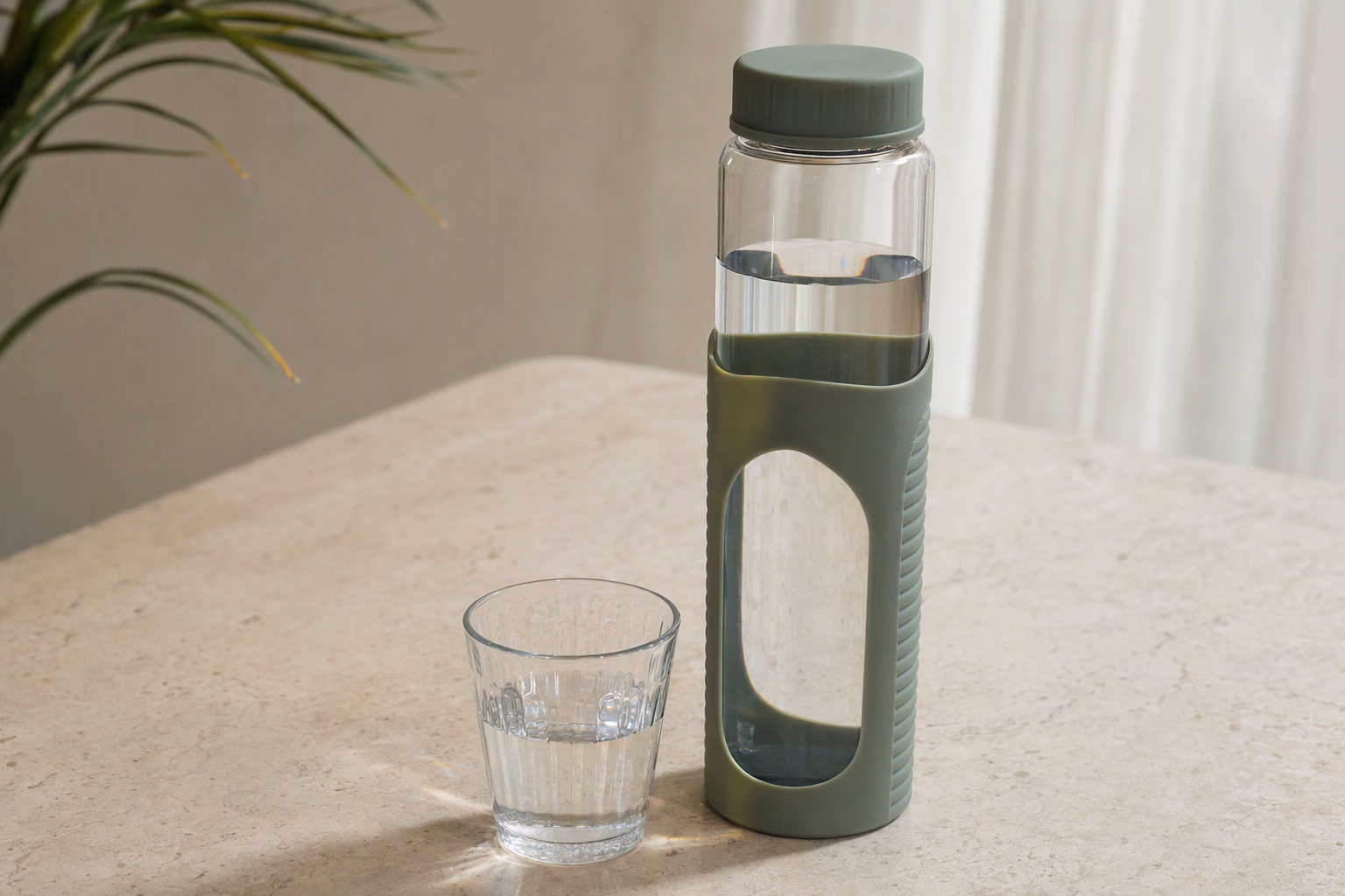 Clear Jolora glass bottle with a sage protective sleeve on a sunlit mineral surface